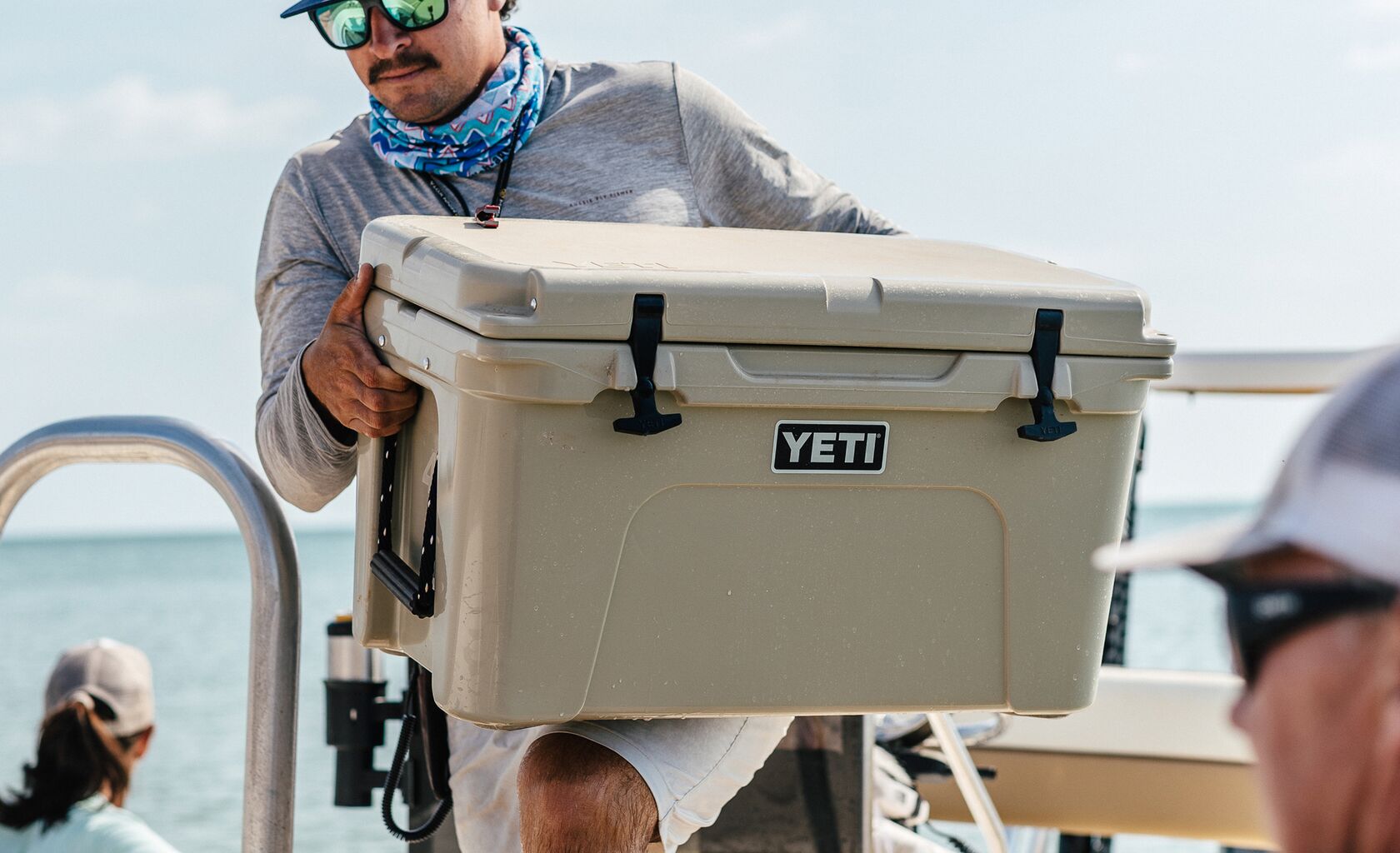 Crew member carrying a tan YETI Tundra cooler aboard a fishing boat